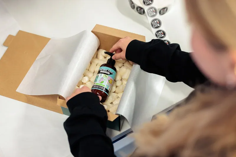 Eine Haarpflegeflasche wird mit Polstermaterial in einen Versandkarton gelegt