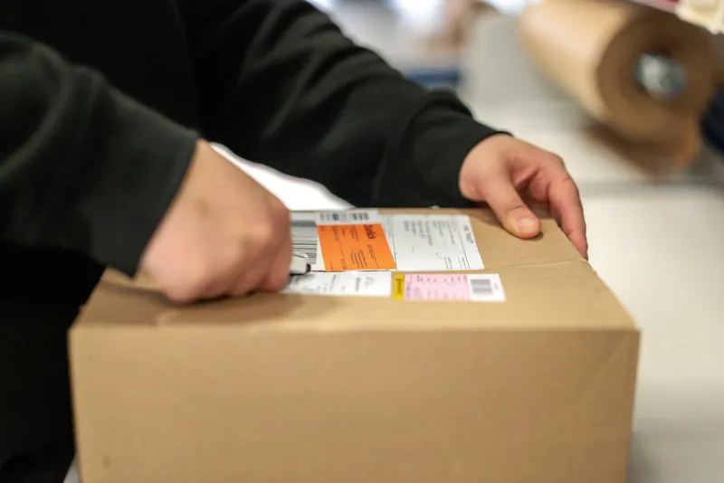 Ein Versandkarton mit Paketetiketten wird am LCR-Arbeitsplatz geöffnet