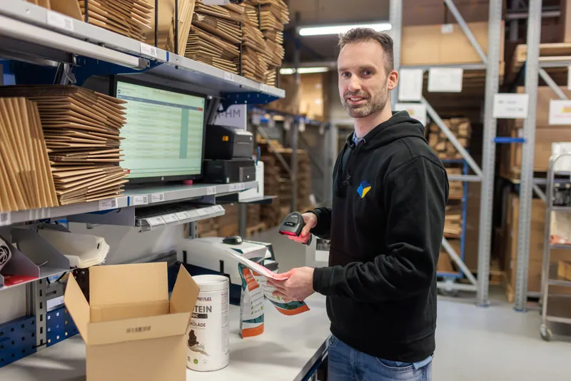 LCR Mitarbeiter am Packplatz mit Supplement-Produkten und Barcodescanner
