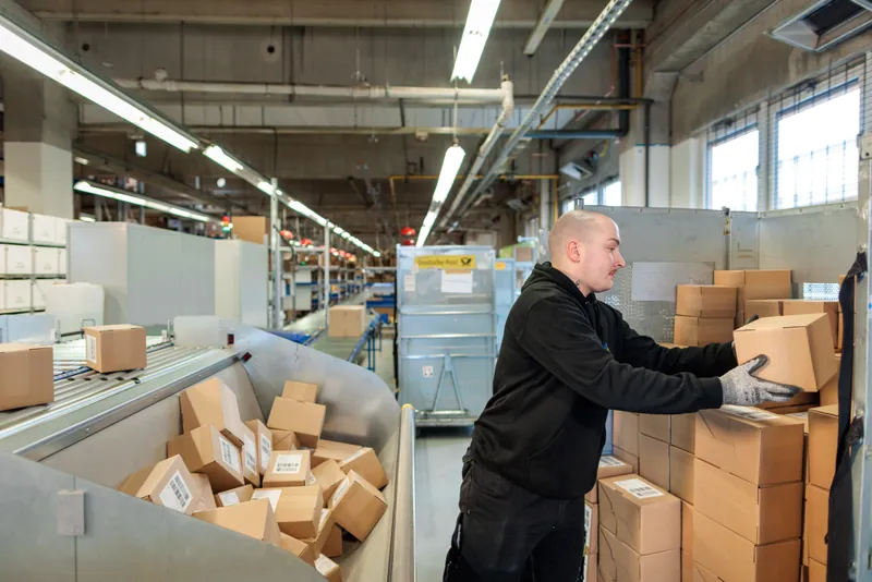 Ein LCR-Mitarbeiter übergibt gepackte Pakete an die Versandstrecke